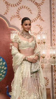 a woman in a white and gold lehenga standing next to a chandelier