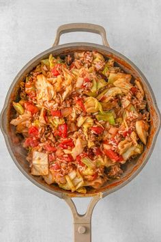 a skillet filled with meat and vegetables on top of a white countertop next to a wooden spatula