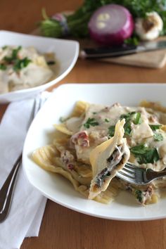 a white plate topped with pasta covered in sauce and cheese next to a fork on top of a wooden table