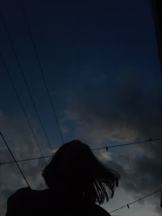 a person standing in front of power lines with the sun behind them and dark clouds