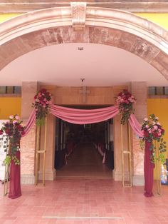 an entrance to a building decorated with pink flowers and greenery on the sidelines