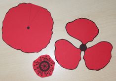 cut out pieces of red paper sitting on top of a wooden table next to a flower