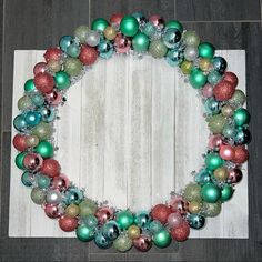 a wreath made out of christmas ornaments on a wooden floor with white boards in the background