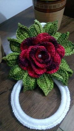 a crocheted flower is on top of a white wreath with green leaves and red flowers