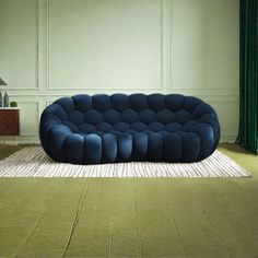 a blue couch sitting on top of a rug in front of a green curtained wall