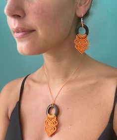 a woman wearing an orange and black necklace with two large pendants on it's sides