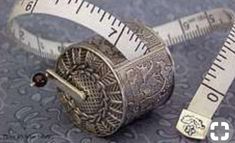 a measuring tape and an old silver thimble are on a blue background with ornate designs