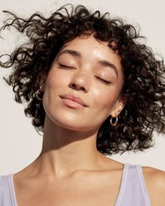 a woman with her eyes closed wearing large gold hoop earrings and a blue tank top