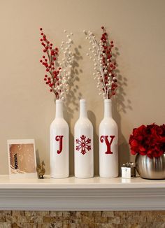 three white vases with red letters and flowers in them on top of a mantel