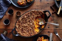 a casserole dish with a serving spoon in it on a wooden table next to other dishes and utensils