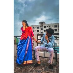 a man sitting next to a woman in a blue and red sari on a bench