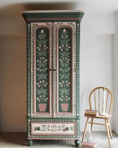 an armoire painted in green and pink with flowers on the door, next to a chair