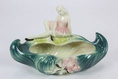 a ceramic figurine sitting on top of a wave shaped bowl with flowers in it