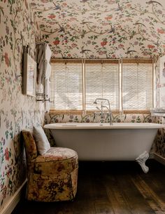 an old fashioned bathtub and chair in a bathroom with floral wallpaper