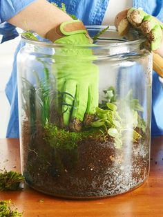 a person wearing green gloves and gardening gloves is in a jar filled with dirt and moss