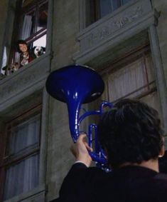 a man playing a blue trumpet in front of a building