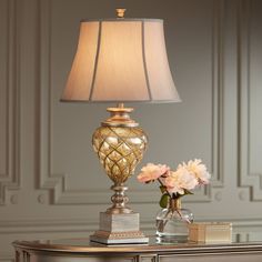 a table lamp sitting on top of a wooden desk next to a vase with flowers