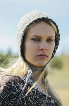 a woman wearing a knitted hat and looking at the camera while standing in a field