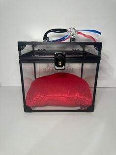 a red pillow in a black case on a white surface with a ribbon around it