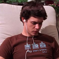 a young man sitting in a chair listening to music on his cell phone and wearing headphones