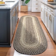 a kitchen with white cabinets and wooden flooring has a large rug on the floor