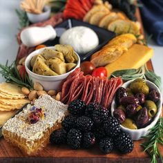 an assortment of food is displayed on a wooden platter with cheese, crackers and fruit