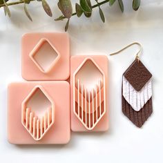 three pieces of jewelry sitting on top of a white table next to a plant with leaves