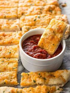 cheesy bread sticks being dipped with marinara sauce in a small white bowl