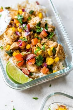 a glass dish filled with rice, chicken and veggies next to a lime wedge