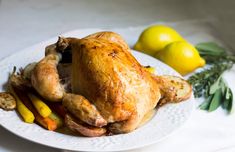 a white plate topped with a cooked chicken and veggies next to lemons