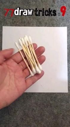 a hand holding several small toothpicks on top of a white piece of paper