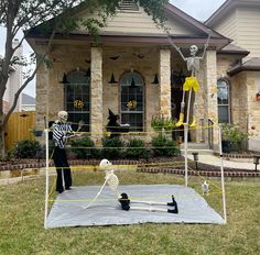 two skeletons playing volleyball in front of a house with halloween decorations on the lawn and outside