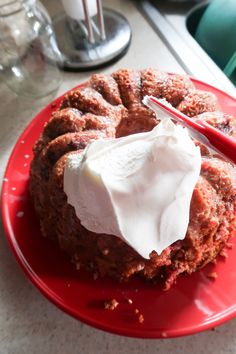 a red plate topped with a bundt cake covered in whipped cream next to a fork