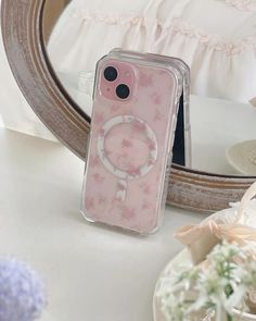 a pink phone case sitting on top of a table next to a flowery vase