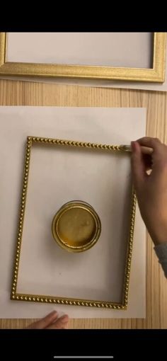 a person is holding a pen and drawing on paper with gold trim around the edges