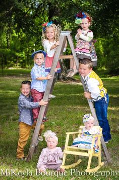 several children are posing for a photo on a wooden ladder in the grass with trees behind them