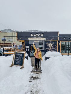 a woman standing in front of a building with snow on the ground and holding her arms up