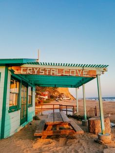 a wooden bench sitting under a green and white awning on top of a sandy beach