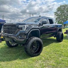 a large black truck parked on top of a lush green field next to a tent