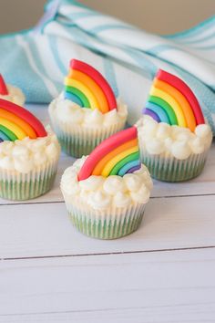 four cupcakes with white frosting and rainbow decorations on them sitting on a wooden table