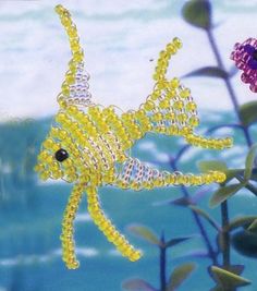 a beaded fish sitting on top of a plant next to the ocean