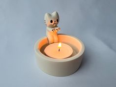 a cat figurine sitting in a bowl with a lit candle