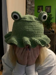 a woman wearing a green crocheted hat covering her face with one eye and the other hand