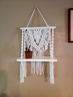 a white macrame hanging from a wall next to a potted plant on a shelf