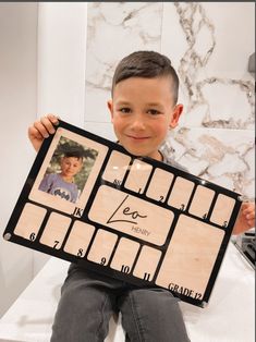 a young boy holding up a wooden board with pictures on it