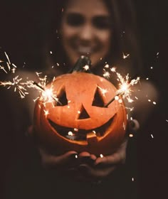 a woman holding a jack o lantern with sparklers