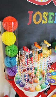 there are many different colored candies on the table with paper plates and cupcakes