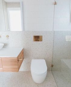 a white toilet sitting next to a sink in a bathroom under a window with a wooden cabinet