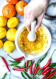 someone is dipping something into a bowl with peppers and lemons around it on the table