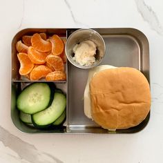 a metal tray with a sandwich, cucumber and orange slices on it next to some other food